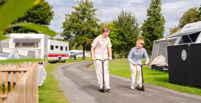 Två barn på sparkcykel på en camping.
